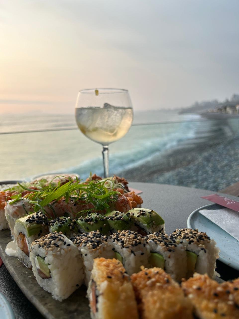 Nikkei sushi and a glass of wine on a table above the Pacific at sunset, Lima